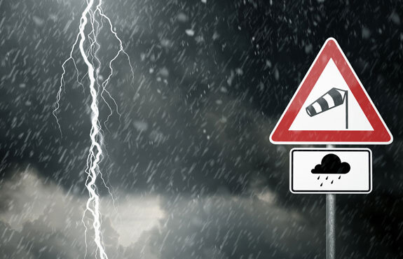 Warnschild für Sturm und Regen vor dunklem Gewitterhimmel mit Blitz und starkem Regen.