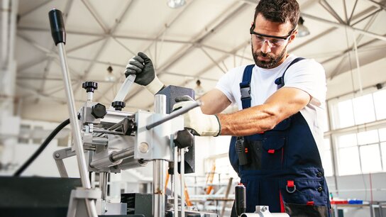 Mann in Arbeitskleidung bedient eine Maschine in einer modernen Werkstatt, umgeben von Werkzeugen und Maschinen.