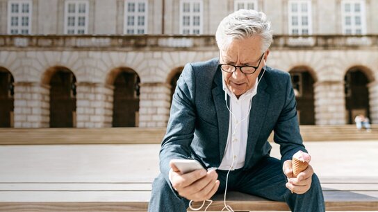 Junge Frau sitzt am Tisch, schreibt auf einer Versandbox und arbeitet mit einem Laptop in einem kreativ gestalteten Raum.