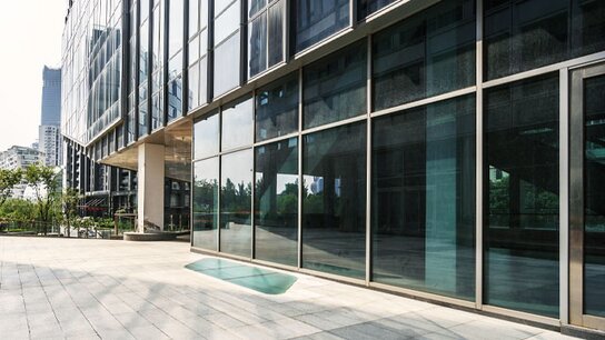 Moderne Glasfassade eines Gebäudes mit einem großzügigen, lichtdurchfluteten Eingangsbereich und angrenzender Grünfläche.