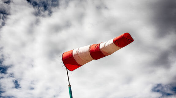 Roter und weißer Windsack weht vor einem wolkigen Himmel.