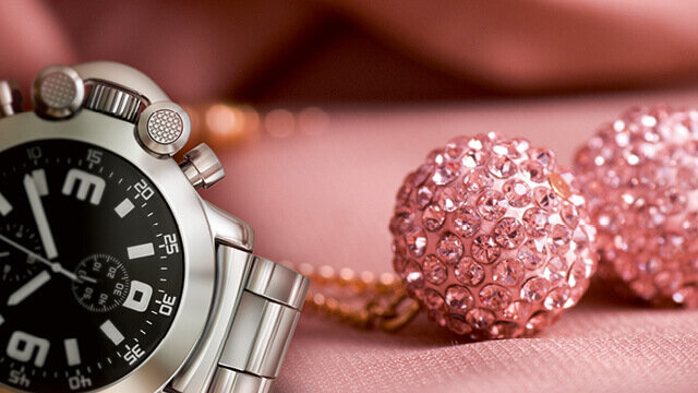 Elegante Armbanduhr aus Edelstahl neben funkelndem, rosa Schmuck auf einem weichen, pinken Hintergrund.