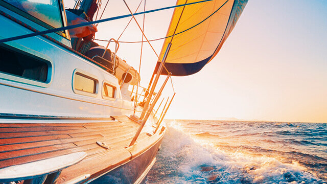Segelboot in der Abenddämmerung, mit aufgeregtem Wasser, wehendem Segel und hellen Farben am Horizont.