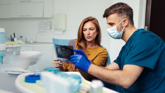 Zahnmedizinische Beratung: Ein Arzt und eine Patientin betrachten gemeinsam eine Röntgenaufnahme in einer modernen Praxis.