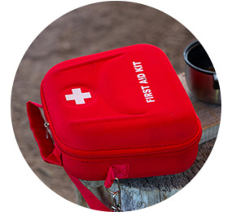 Rote Tasche mit dem Aufdruck „FIRST AID KIT“ und weißem Kreuz, auf einem Holzuntergrund platziert.