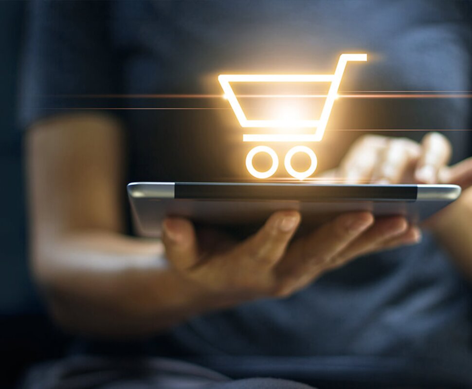 Eine Person hält ein Tablet mit einem leuchtenden Einkaufswagen-Symbol, das Einkaufsaktivität symbolisiert.