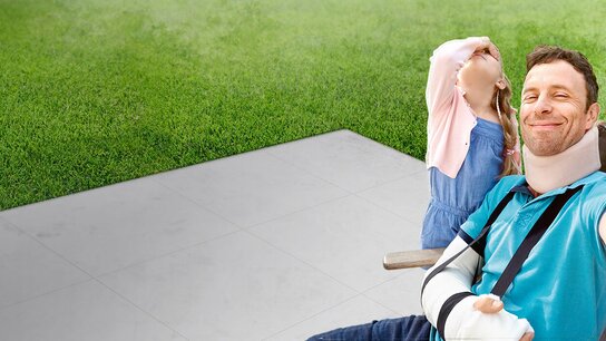 Lächelnder Mann mit Hals- und Armverband, der mit einem Kind im Hintergrund, das den Kopf zurückwirft, ein Selfie macht.