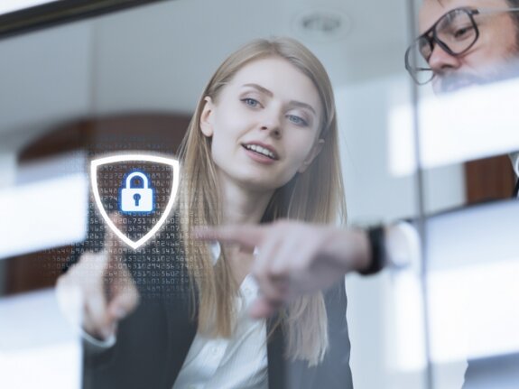 Zwei Personen zeigen auf ein digitales Schloss-Symbol auf einem Bildschirm in einem modernen Büroraum.