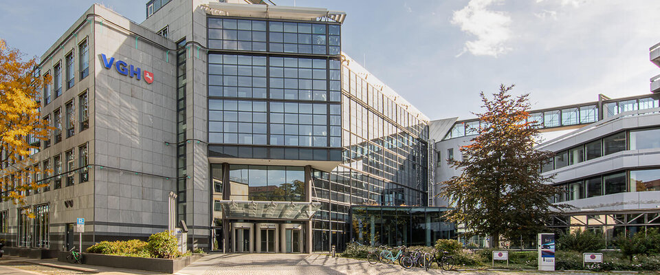 Moderne Bürogebäude mit großen Glasfassaden, Eingangsbereich, umgeben von Bäumen und Fahrrädern im Vordergrund.