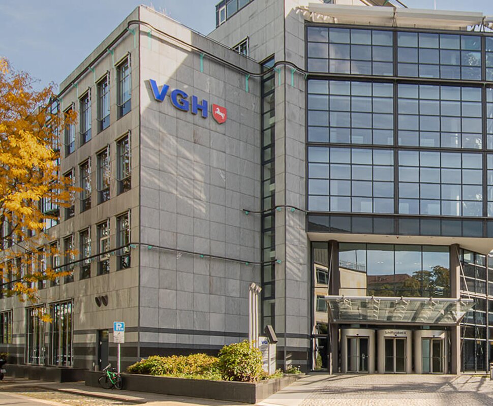 Moderne Bürogebäude mit großen Glasfassaden, Eingangsbereich, umgeben von Bäumen und Fahrrädern im Vordergrund.