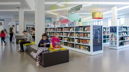 Moderne Bibliothek mit Lesebereichen, Regalen voller Bücher und mehreren Besuchern, die lesen oder lernen.