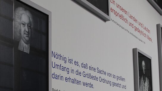 Porträts historischer Persönlichkeiten mit informativen Texten und Zitaten auf einer ausstellungsähnlichen Wand.