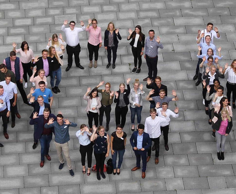 Gruppendynamik mit mehreren Personen, die fröhlich posieren und „NOW“ auf dem Boden bilden.