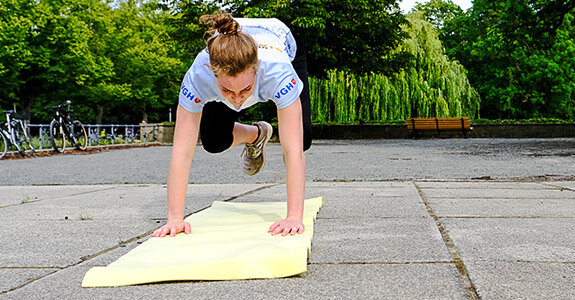 Eine Person führt eine Sportübung in einem Park auf einer Matte aus, umgeben von Bäumen und abgestellten Fahrrädern.