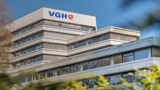 Modernes Gebäude der VGH mit mehreren Etagen, umgeben von grünen Bäumen und klarem Himmel.