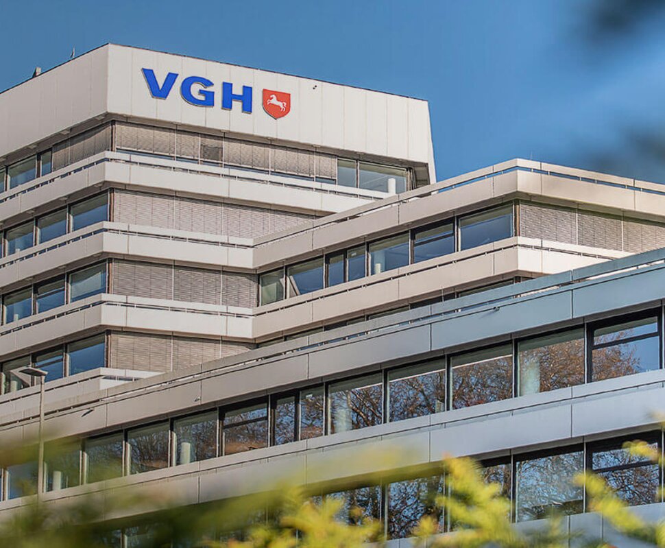 Modernes Gebäude der VGH mit mehreren Etagen, umgeben von grünen Bäumen und klarem Himmel.